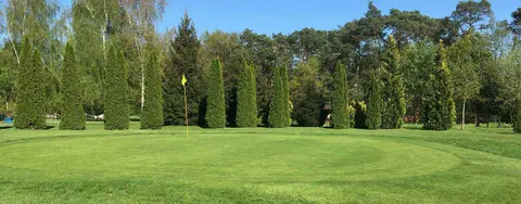 Gepflegtes Grün mit gelber Fahne vor einer Reihe hoher Säulenkoniferen auf dem Golfplatz Mahlow