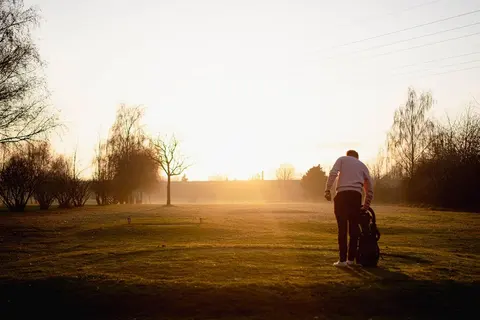 Golfer mit Tragebag auf dem Fairway im Gegenlicht der untergehenden Sonne