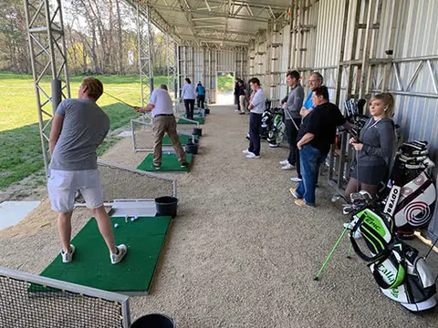 Überdachte Abschlagplätze der Driving Range mit Golfern in Trainingsposition