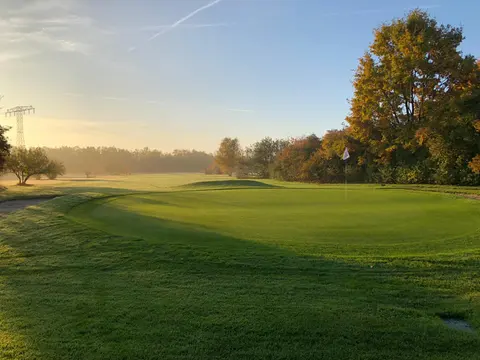 Morgenlicht über einem Grün des Golfclub Mahlow, dahinter Herbstbäume und leichter Nebel über dem Fairway
