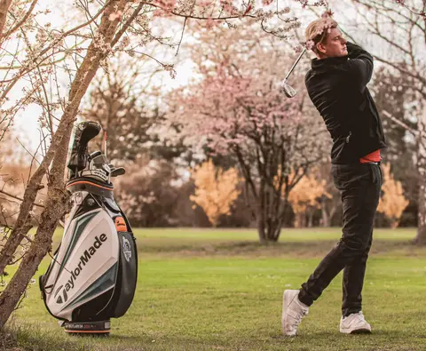 Golfer im Schwung-Finish neben seinem Golfbag auf einer Rasenfläche