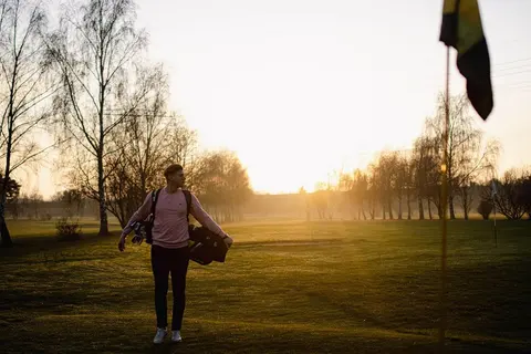 Golfer mit Tragebag geht im Abendlicht über das Fairway in Mahlow